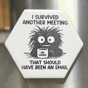 A white ceramic hexagon tile magnet engraved with a frazzled creature holding a mug that says NO WORK and the text I Survived Another Meeting That Should Have Been An Email