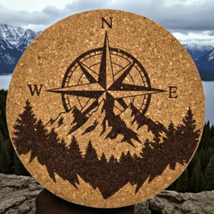 Round natural mountain compass cork coaster with a detailed laser-engraved compass rose, mountain peaks, and pine forest design.