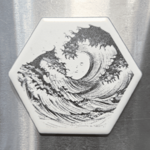 A white hexagon ocean wave ceramic magnet featuring a detailed black illustration of a cresting ocean wav