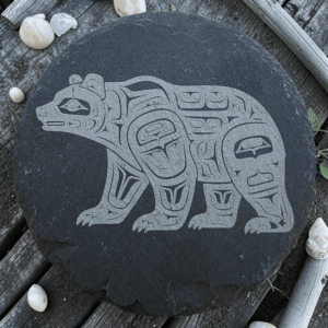 Round dark slate coaster featuring an etched Pacific Northwest Indigenous style bear design