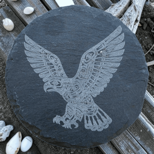 Round dark slate coaster featuring an etched Pacific Northwest Indigenous style eagle in flight