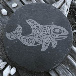 Round dark slate coaster featuring an etched Pacific Northwest Indigenous style orca