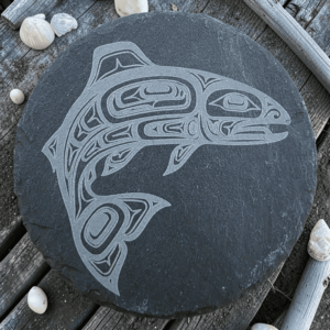 Round dark slate coaster featuring an etched Pacific Northwest Indigenous style salmon design