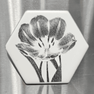 A white hexagonal tulip tile magnet featuring a dark, detailed floral laser engraving of three blooming tulips.