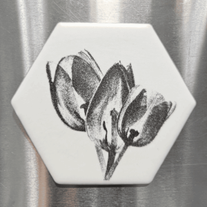 A white hexagonal tulip tile magnet featuring a dark, detailed floral laser engraving of three blooming tulips.