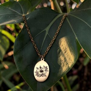 An oval metallic pendant featuring an engraved hibiscus necklace